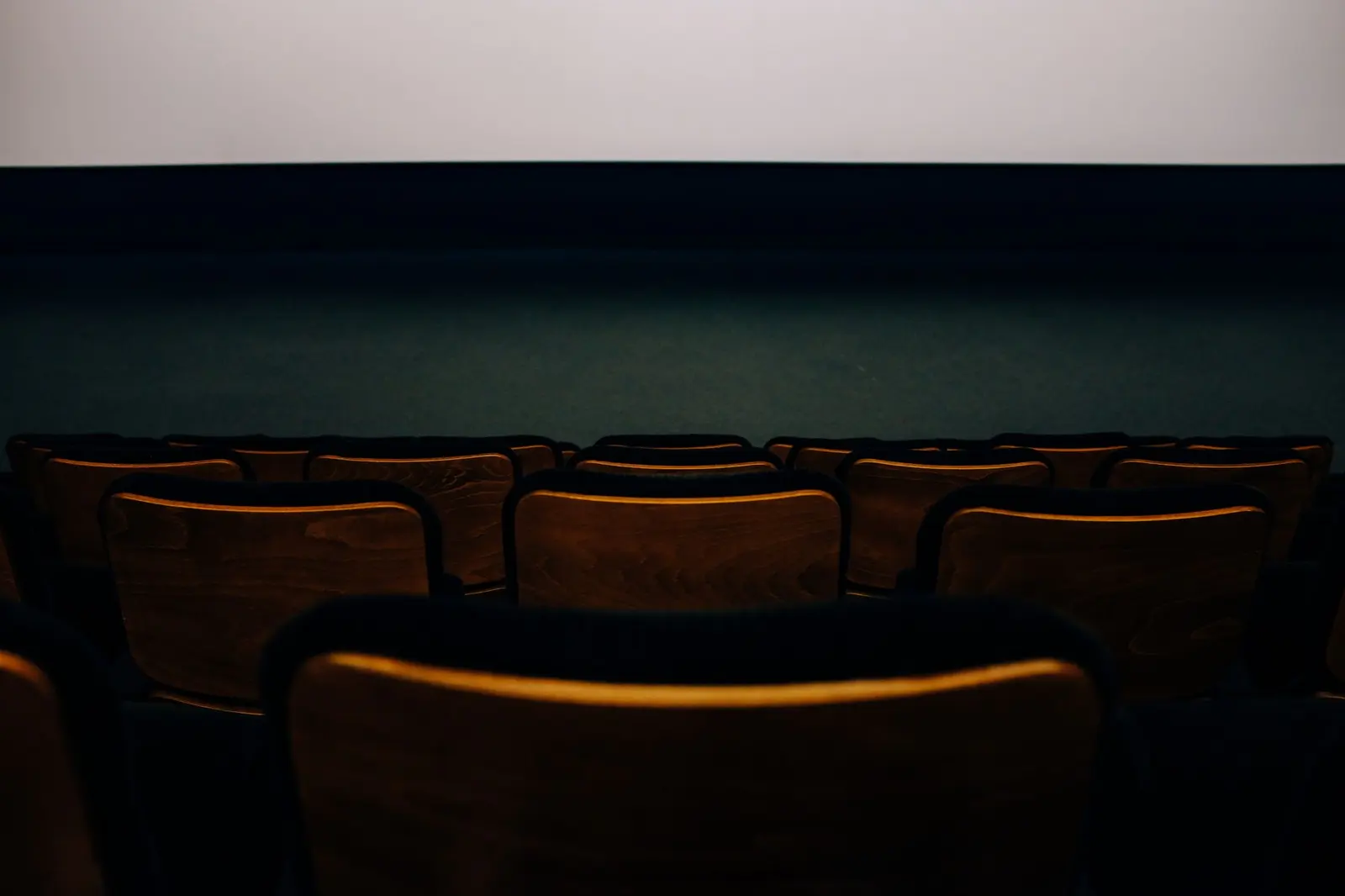 Auditorio vacío con butacas de madera frente a una pantalla
